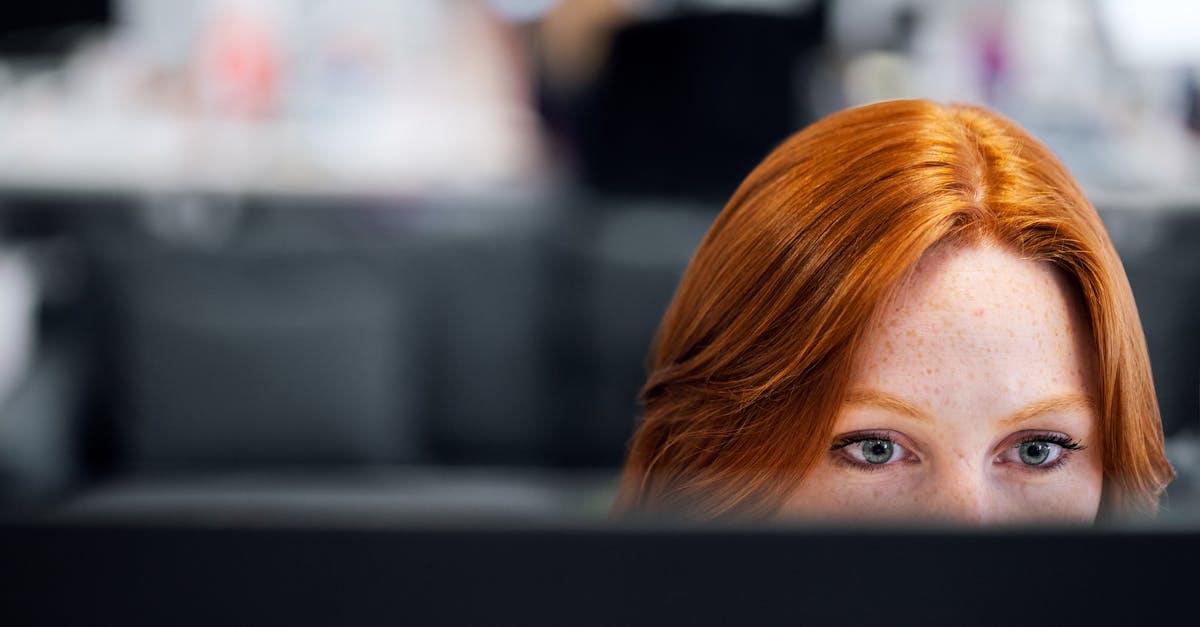 A woman with red hair intensely focused on a computer screen in an office setting.
